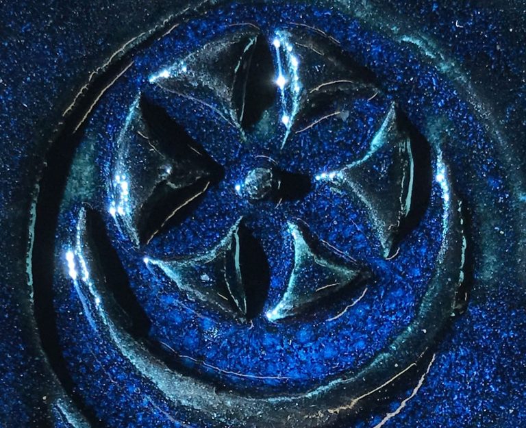 Image of a flower-impressed clay tile with mottled light and dark blue glaze