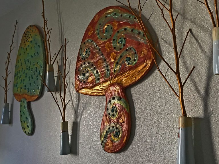 Detail view of an installation of multicolored mushrooms with red, white, and blue vessels with gold twigs.
